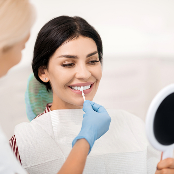 Cosmetic dentist holding a veneer in front of a smiling patient's tooth