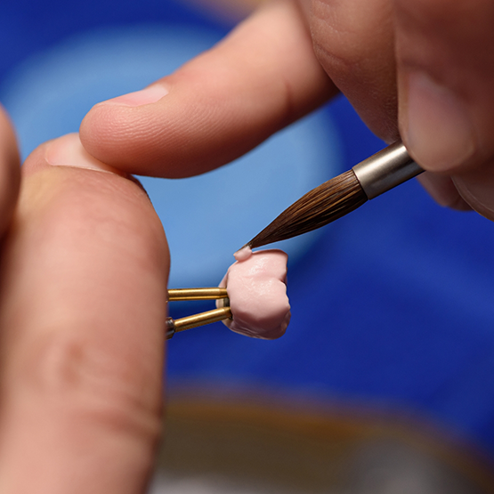 Close up of a person paining a dental crown with a tiny brush