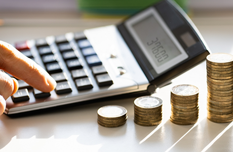 Person typing on a calculator next to stacks of coins