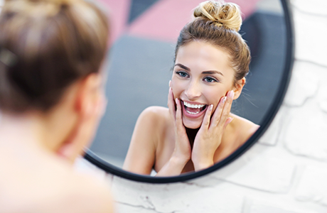 Smiling woman looking in a mirror and touching her face