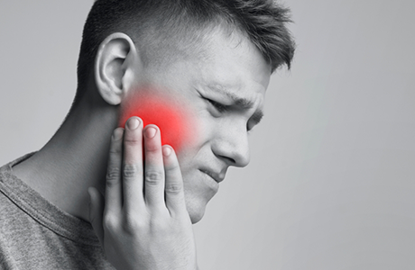 Man wincing in pain while holding the side of his cheek