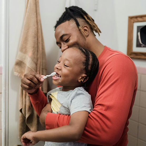 Father helping his young child brush their teeth