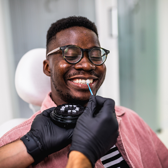 Man smiling while his dentist holds a veneer in front of his tooth