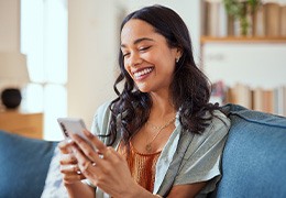 Woman smiling while scrolling on phone on couch