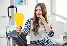 Smiling female dental patient looking in mirror