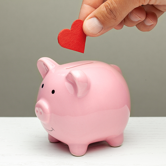 Hand placing a red paper heart in a piggy bank