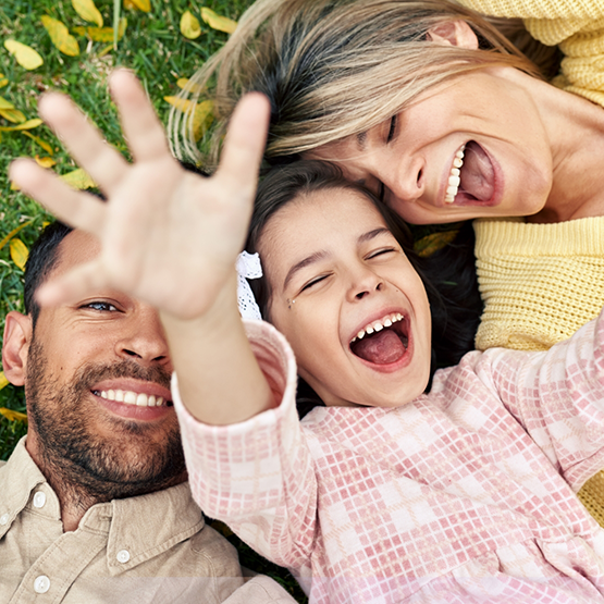 Family of three smiling while laying in the grass