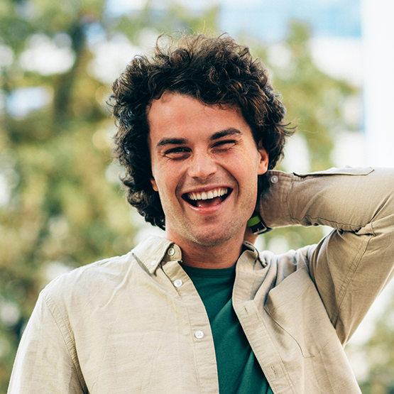 Man with fluffy brown hair smiling outdoors after replacing missing teeth in Goodlettsville