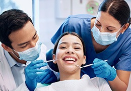 Dentist and dental assistant examining smiling patient's teeth