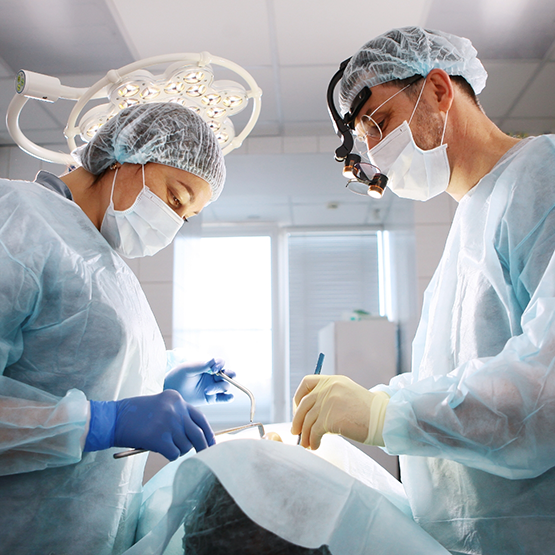 Two dental professionals performing wisdom tooth extractions on a patient