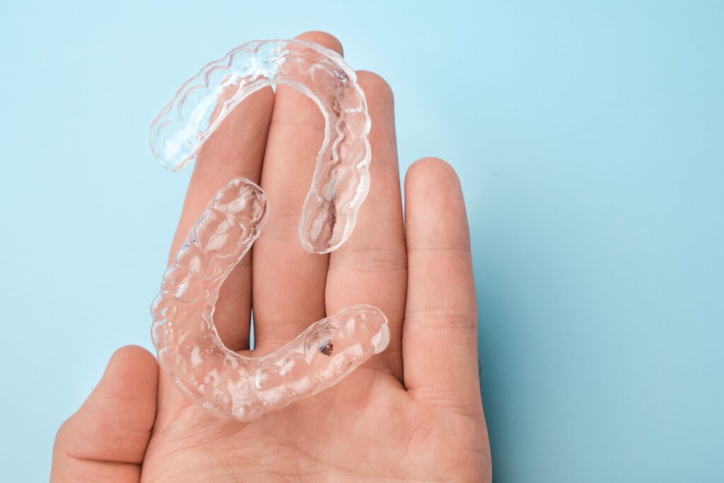 Two clear aligners resting on a hand with a light blue background